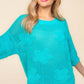 Woman wearing a teal floral crochet side slit knit top with jeans, showcasing the stylish and feminine floral crochet design.