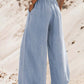 Woman in medium blue drawstring wide leg jeans, showcasing comfort and style against a sandy backdrop.