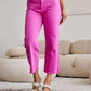 Model wearing Crop Chloe Full Size Tummy Control High Waist Raw Hem Jeans in bright pink, standing in a modern living room. RFM Jeans.