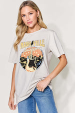 Woman wearing a Graphic Round Neck Short Sleeve T-Shirt featuring a Nashville guitar design, paired with blue jeans.