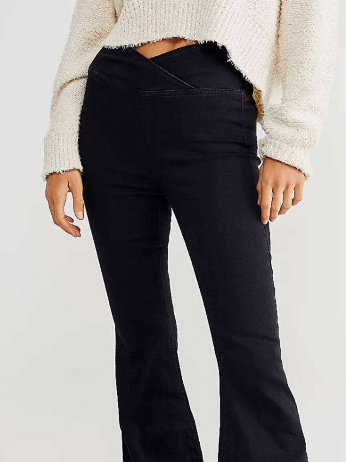 Woman wearing black Asymmetric Waist Flare Jeans with unique waistline design, paired with a cozy white sweater.