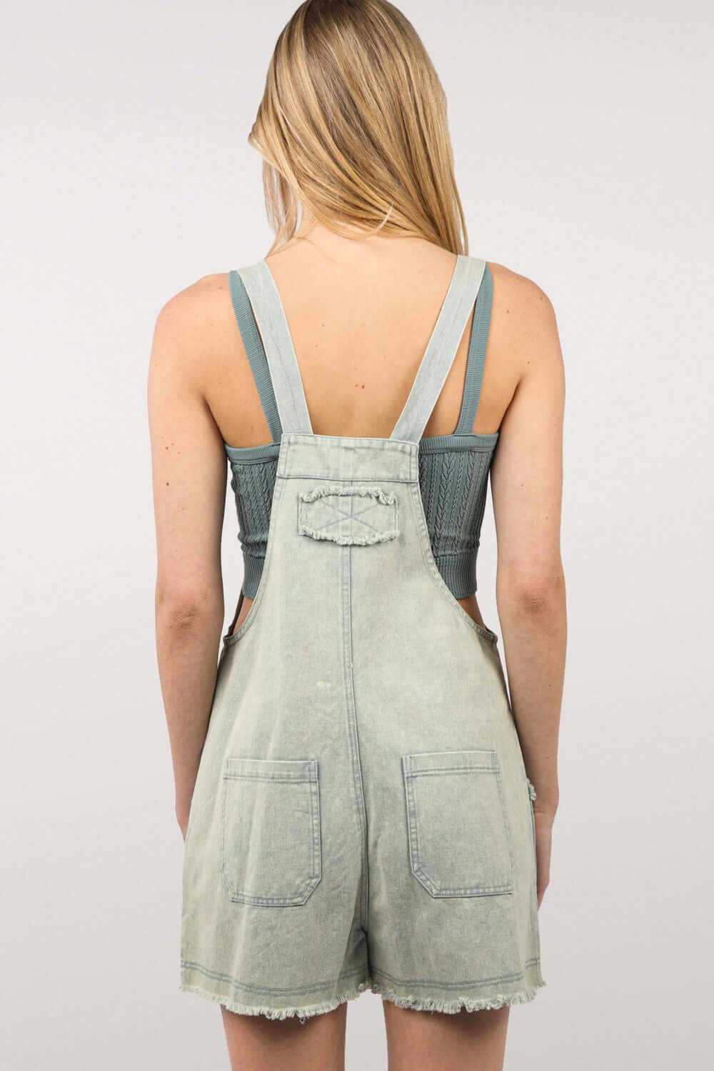 Back view of woman wearing washed frayed hem denim overall romper with side and back pockets, showcasing vintage and eco-friendly casual fashion.