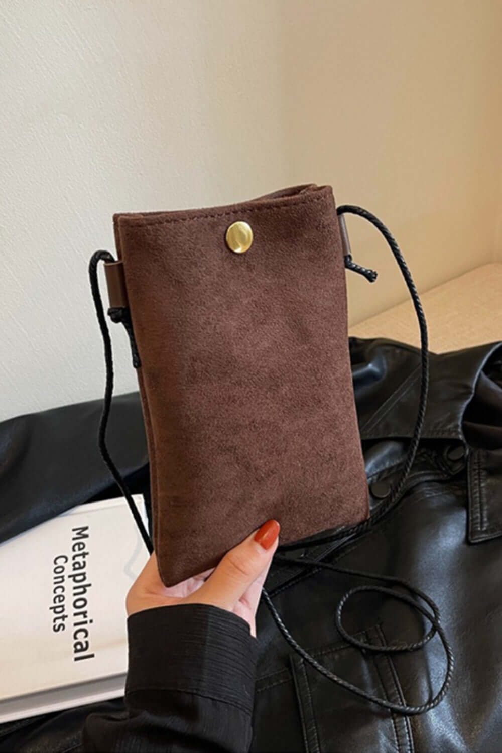 Bella Road Suede Snap Down Crossbody Bag in brown held by a hand, featuring a snap-down design and crossbody strap for hands-free convenience.