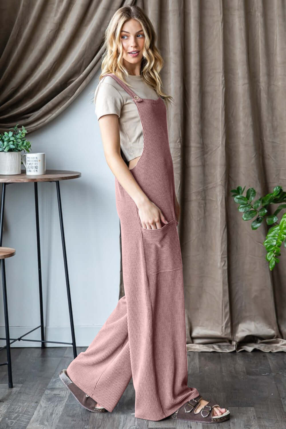 Woman wearing a stylish Ribbed Front Pocket Sleeveless Jumpsuit in a room with modern furniture and plants.