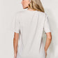 Woman wearing MAMA round neck short sleeve t-shirt in beige, back view, paired with blue jeans.