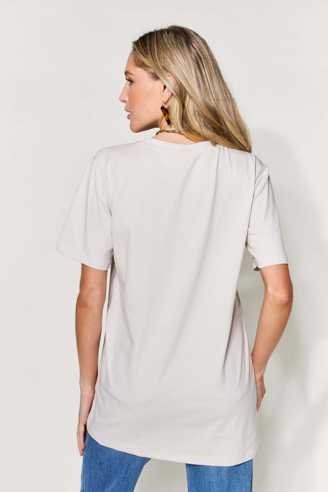 Woman wearing MAMA round neck short sleeve t-shirt in beige, back view, paired with blue jeans.