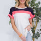 Woman wearing Color Block Round Neck Short Sleeve T-Shirt in pink, white, and navy blue, paired with light jeans and a hat, standing near a plant.