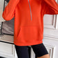 Woman wearing Ivy Lane Half Zip Raglan Sleeve Sweatshirt in bright orange with front pocket and black shorts.