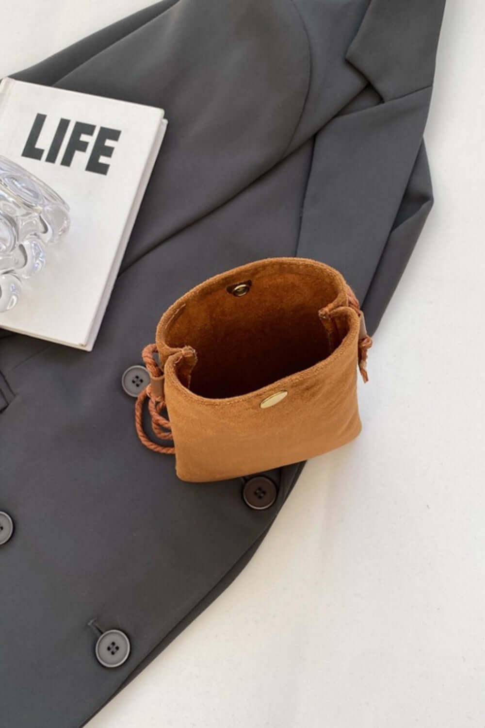 Bella Road Suede Snap Down Crossbody Bag on gray blazer, next to LIFE magazine and clear eyeglasses.