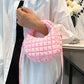 Woman holding a small pink quilted puffy crossbody bag with a removable strap, styled as a clutch against a white shirt backdrop.