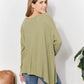 Woman wearing oversized super soft rib layering top with sharkbite hem and round neck, in sage green color, viewed from the back.