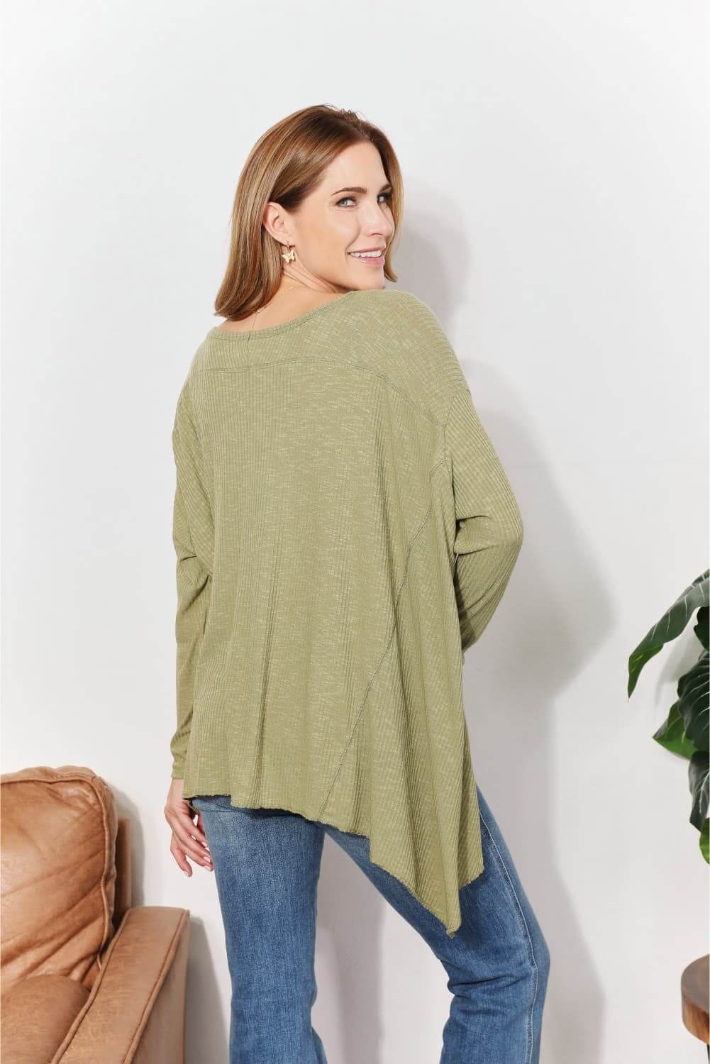 Woman wearing oversized super soft rib layering top with sharkbite hem and round neck, in sage green color, viewed from the back.