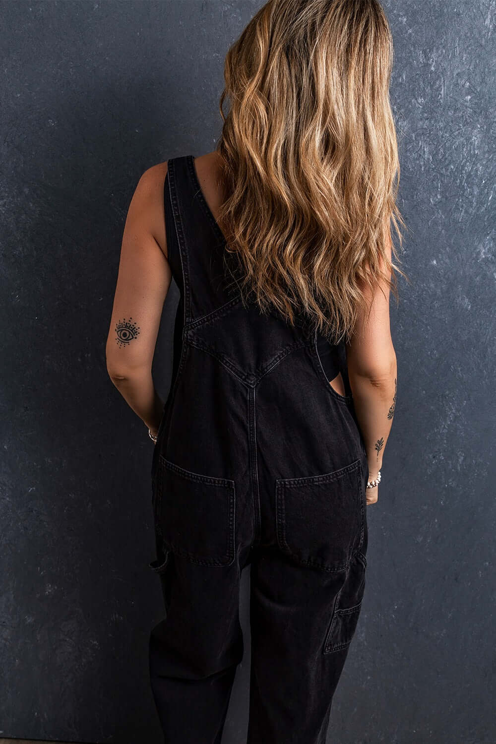 Rear view of woman wearing pocketed straight denim overalls with no stretch, featuring back pocket details.