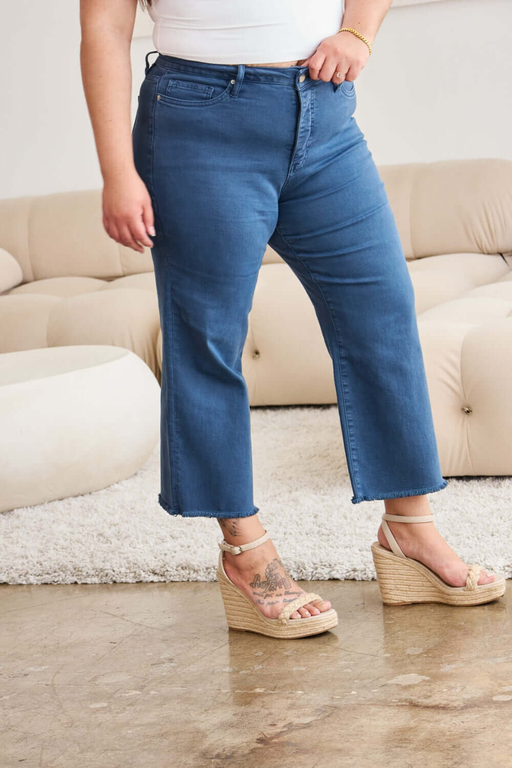 Woman wearing Crop Chloe Full Size Tummy Control High Waist Raw Hem Jeans (RFM Jeans) standing indoors.