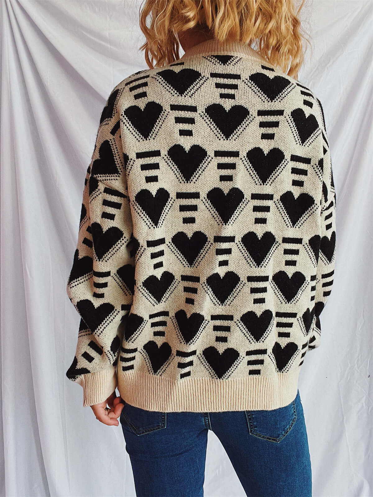 Woman wearing Bella Road Heart Contrast Long Sleeve Dropped Shoulder Sweater with heart pattern, standing against white backdrop