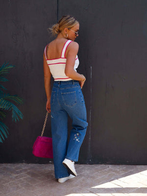 Woman wearing embroidered straight jeans with pockets, white top, and pink purse.