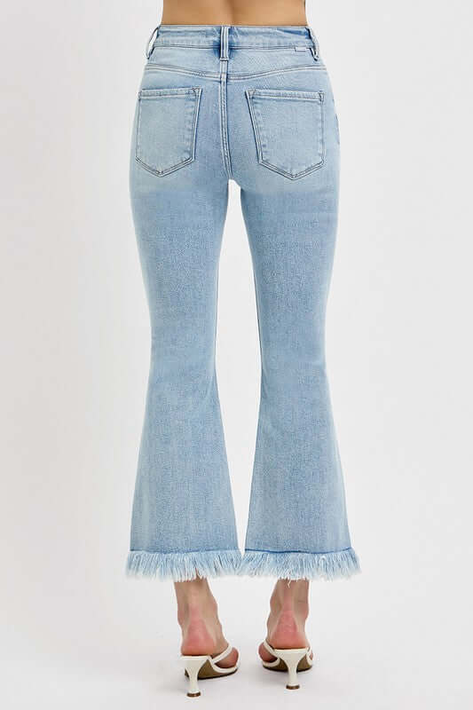 Back view of RISEN plus size raw hem distressed cropped flare jeans in light blue.