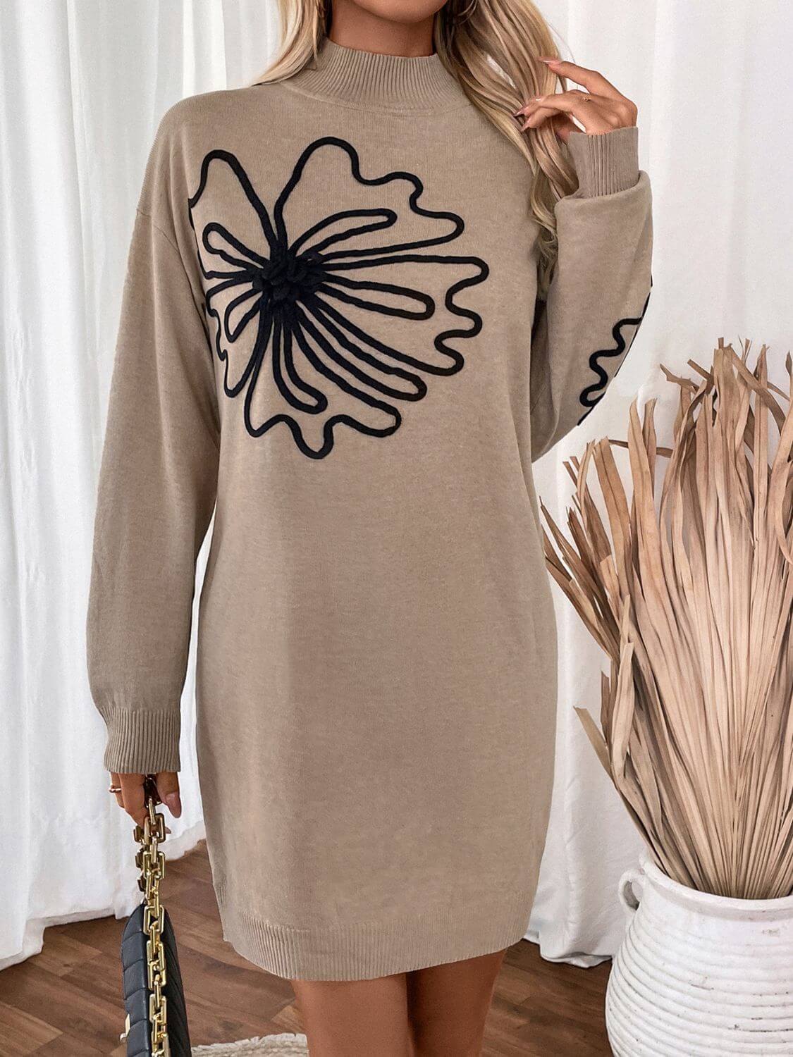 Woman wearing Perfee Flower Mock Neck Long Sleeve Sweater Dress in beige with black floral design, standing beside dried plants.