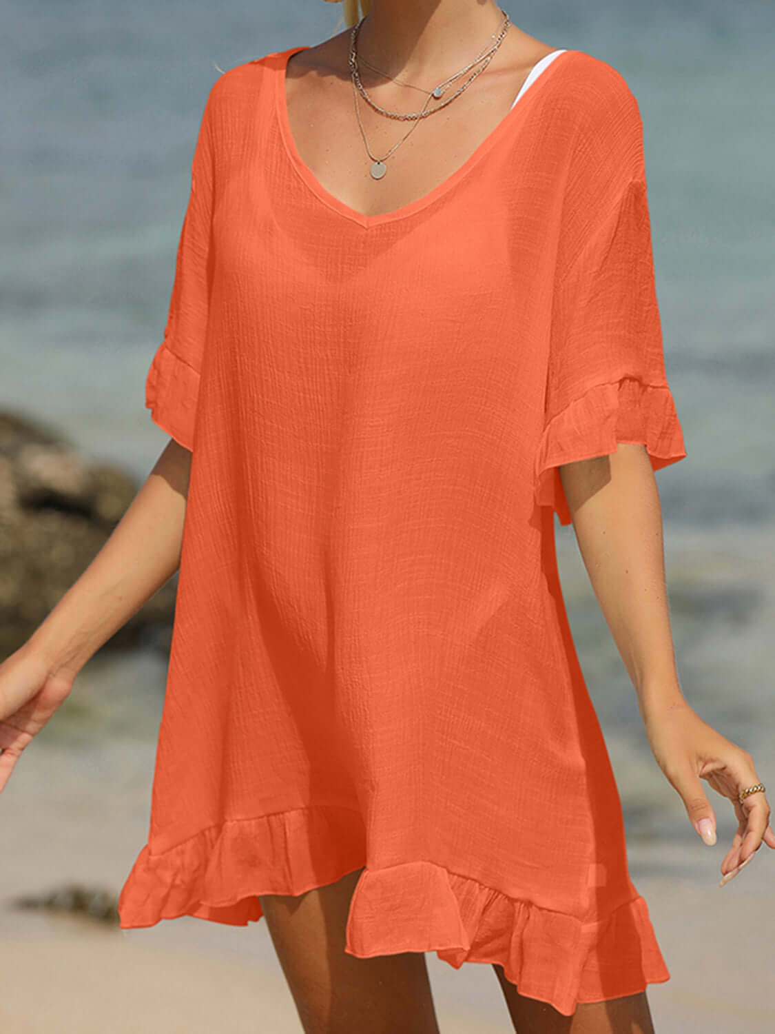 Woman wearing an orange tied ruffled half sleeve cover-up made of 65% cotton and 35% polyester on a beach.