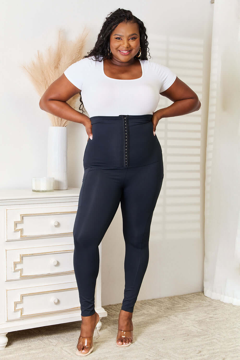 Woman wearing Heimish full size waist trainer corset leggings, showcasing high-performance support and sleek hourglass silhouette in a white top.