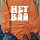 Bella Road Hey Boo Graphic Round Neck Long Sleeve Sweatshirt in orange with Halloween ghost design, paired with jeans and boots.