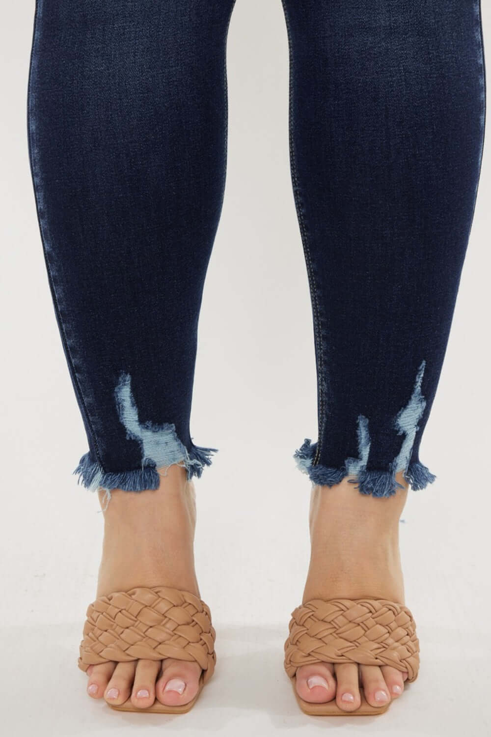 Close-up of Cat's Whiskers Raw Hem High Waist Jeans with frayed detailing at the ankles, paired with woven sandals.