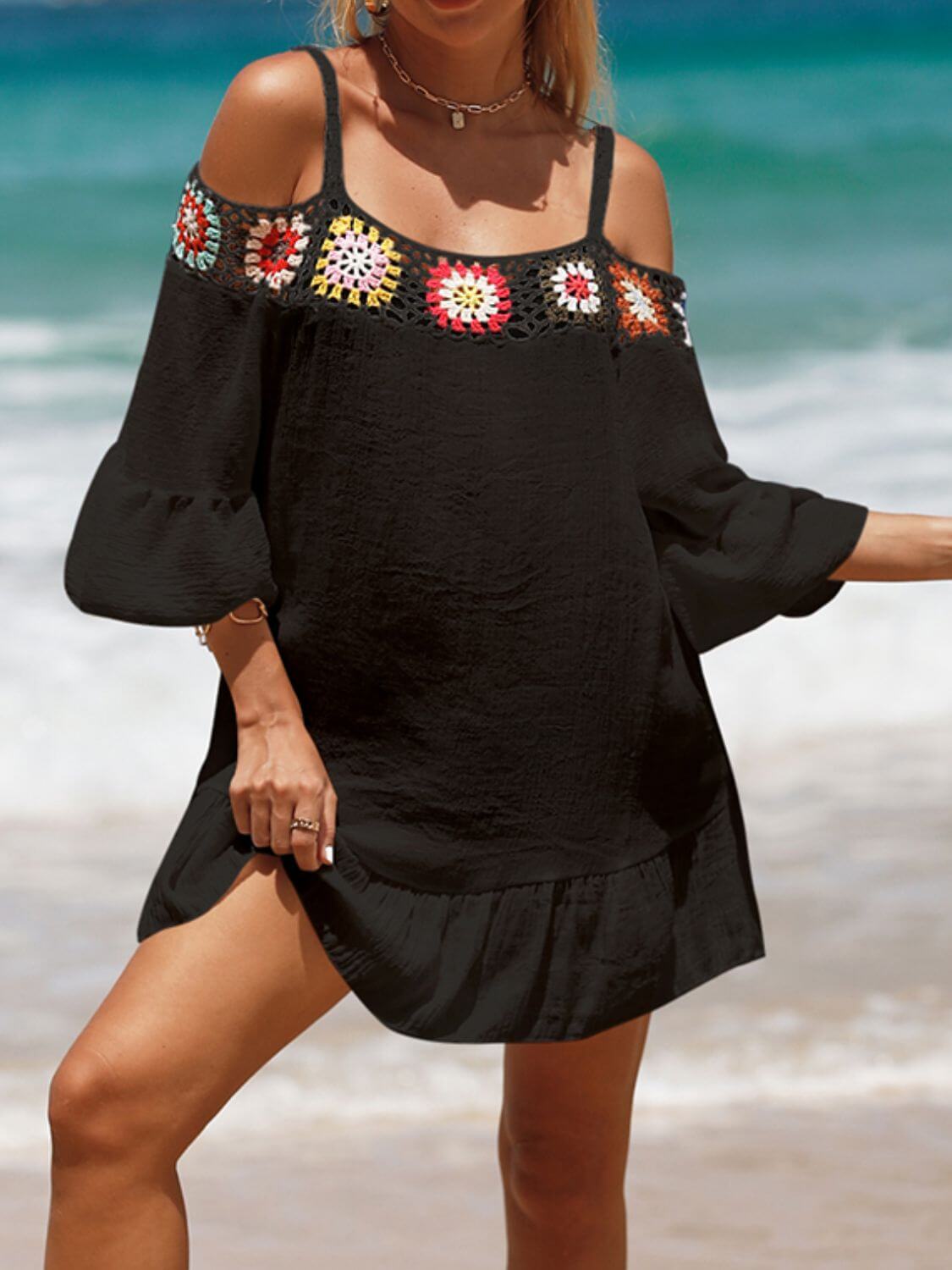 Woman wearing a black crochet cold shoulder three-quarter sleeve cover up on the beach with colorful floral detailing