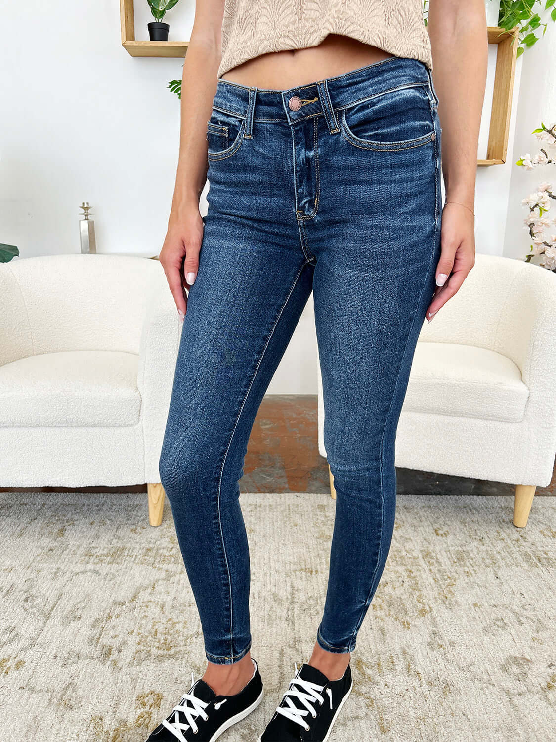 Woman wearing Classic Handsand Skinny Jeans by Judy Blue Jeans standing in a stylish living room.