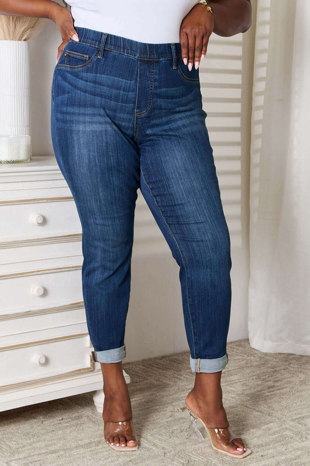 Woman wearing Judy Blue skinny cropped jeans with moderate stretch, styled with clear heels, standing in a modern room.