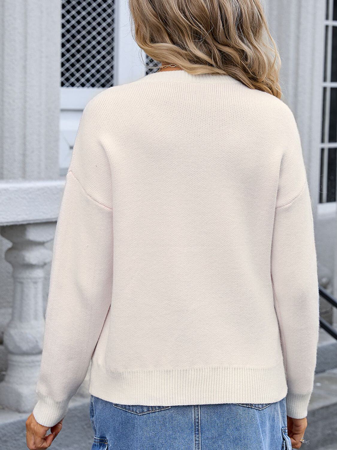 Back view of a woman wearing an Angel Wings Bow Graphic Round Neck Long Sleeve Sweater in a light color, paired with denim jeans.