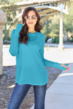 Woman modeling a teal round neck long sleeve t-shirt paired with jeans outdoors