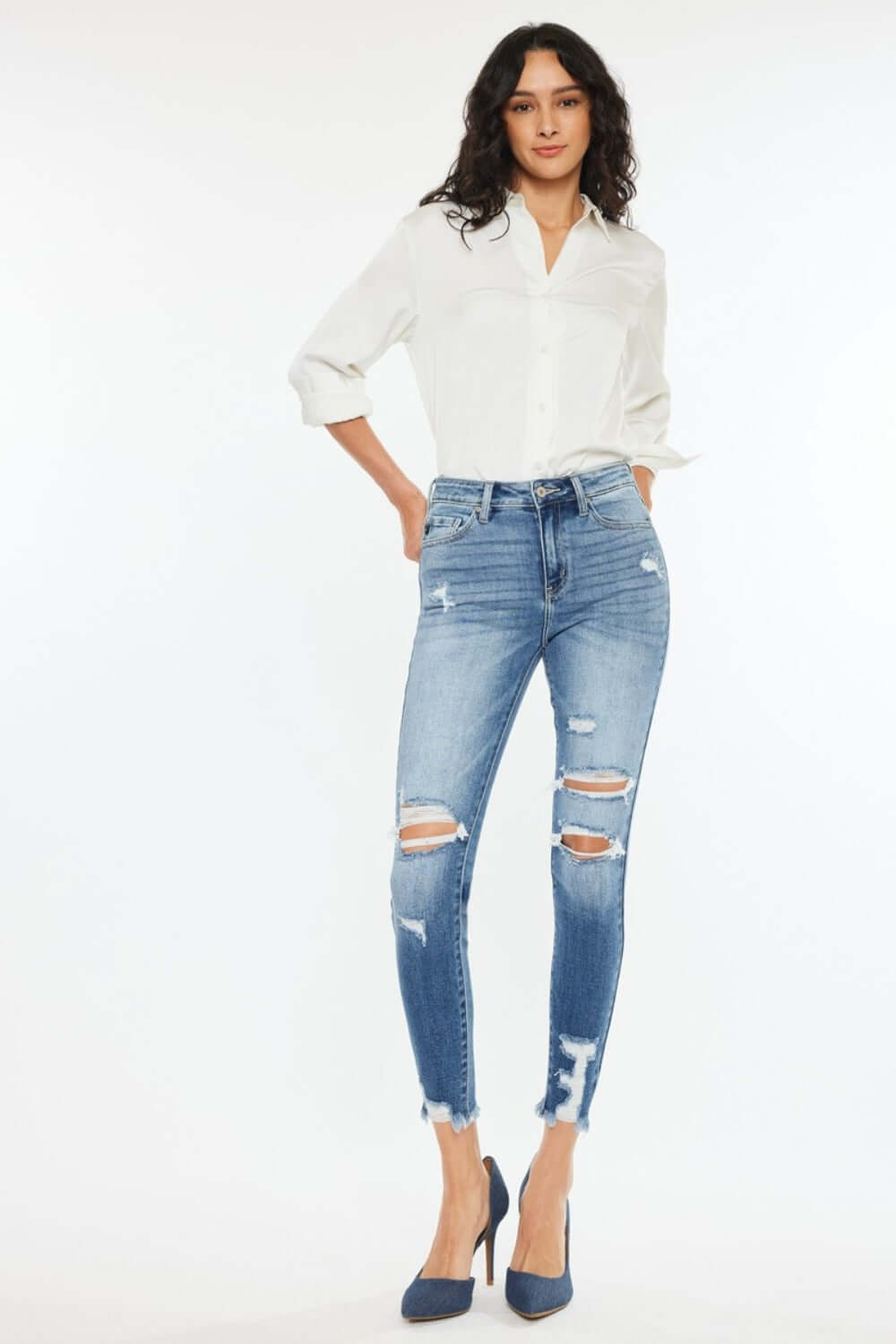 Woman wearing High Rise Frayed Ankle Skinny Jeans in medium wash with distressed detailing and frayed hem, paired with white shirt and heels