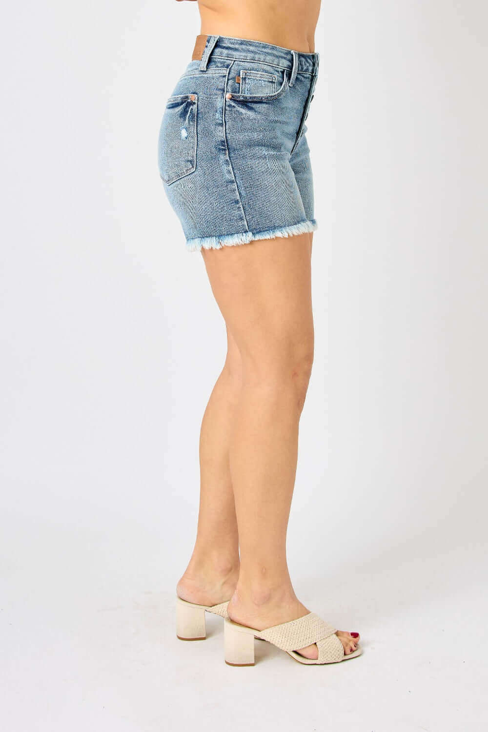 Side view of model wearing Button Fly Raw Hem Denim Shorts by Judy Blue Jeans