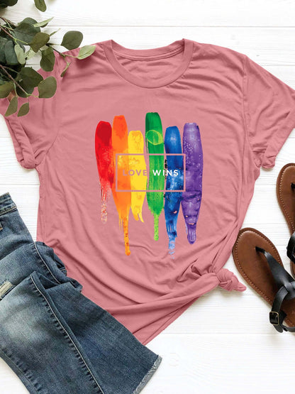 Pink graphic round neck short sleeve T-shirt with rainbow "Love Wins" design, paired with denim jeans and sandals placed beside.