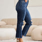 Woman wearing RFM Jeans Crop Dylan Full Size Tummy Control Distressed High Waist Raw Hem Jeans with white heels in a stylish room