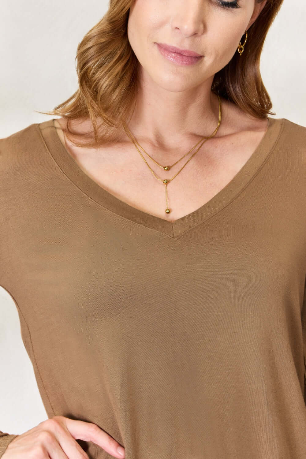 Woman wearing luxurious rayon long sleeve V-neck top in a neutral color, showing close-up detail of neckline and fabric texture.