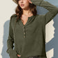 Woman wearing a Double Take Full Size Notched Thumbhole Long Sleeve T-Shirt in olive green with a hat, posing outdoors.