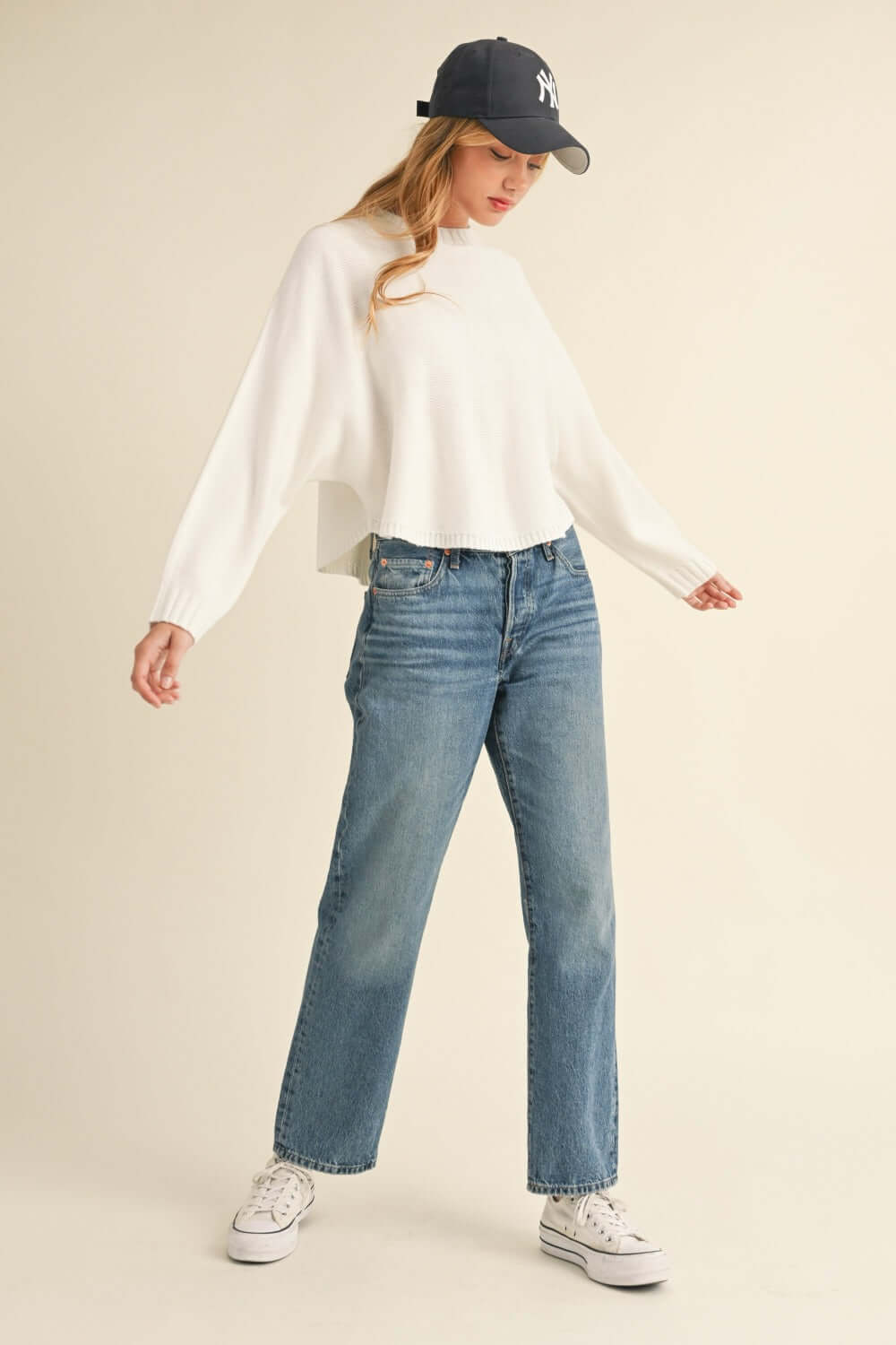 Woman wearing Bella Road Mable Round Neck Dolman Sleeve Cropped Sweater with jeans and a cap, posing in casual outfit