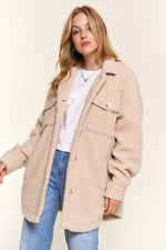 Woman wearing beige teddy sherpa button-down shacket with curved hem, styled over white top and jeans for a cozy casual look.