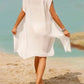 Woman in white Bella Road Swim Cover-Up walking on the beach, showcasing a stylish, sheer design perfect for summer fun.