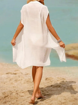 Woman in white Bella Road Swim Cover-Up walking on the beach, showcasing a stylish, sheer design perfect for summer fun.