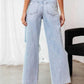 Woman wearing Bella Road distressed wide leg jeans with pockets, back view, showing no-stretch light blue denim fabric.