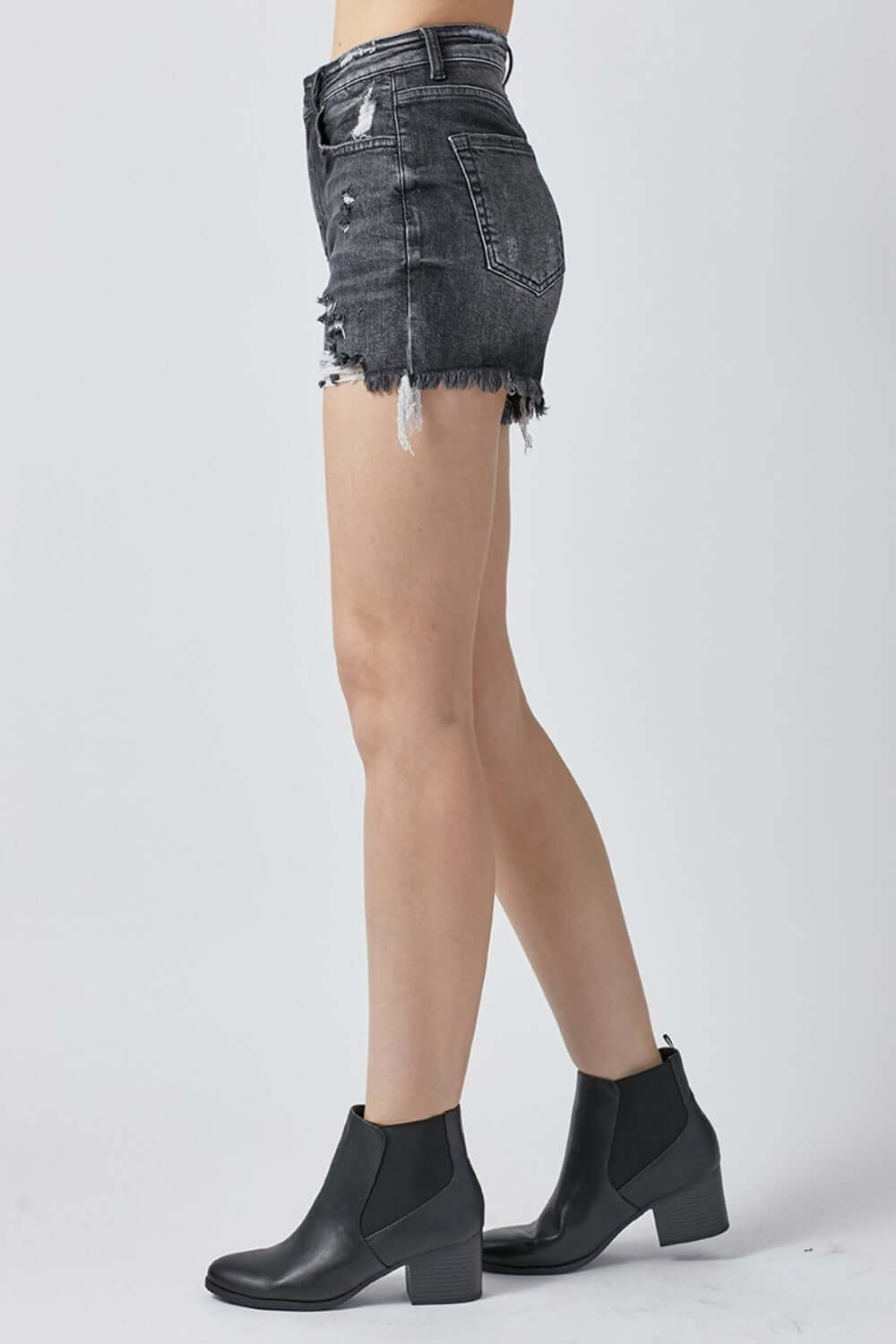 Side view of model wearing high rise distressed denim shorts and black ankle boots by Risen Jeans, perfect for summer wardrobe.