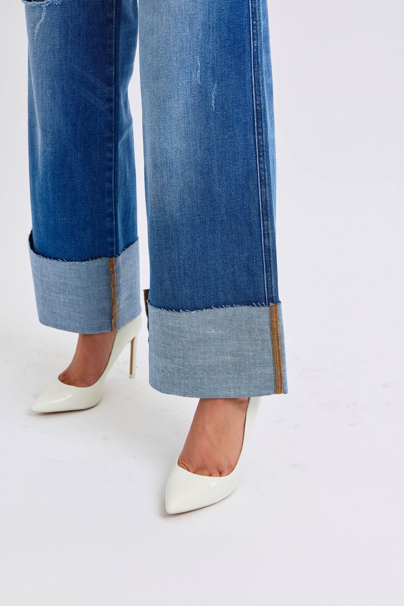 Distressed high waist wide leg jeans with folded cuffs, paired with stylish white stiletto heels on a light background.