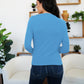 Woman wearing French Blue FAM-FAM Ruched Mock Neck Long Sleeve T-Shirt, standing in a cozy living room setting.