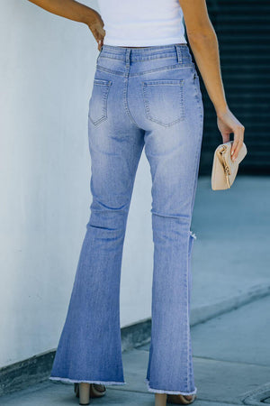 Back view of a woman wearing Bella Road Button-Fly Distressed Raw Hem Flare Jeans in light blue, holding a beige purse.