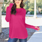 Woman wearing a round neck long sleeve t-shirt in vibrant pink with blue jeans, posing outdoors on a sunny day.