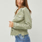 Stylish woman wearing a cropped green raw hem button-up denim jacket with jeans, showcasing trendy fashion vibes.