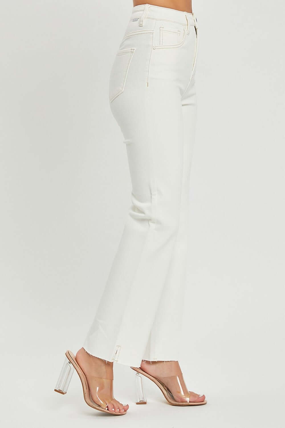 High-rise white jeans with tummy control and raw hem, styled with clear heels for a chic look.