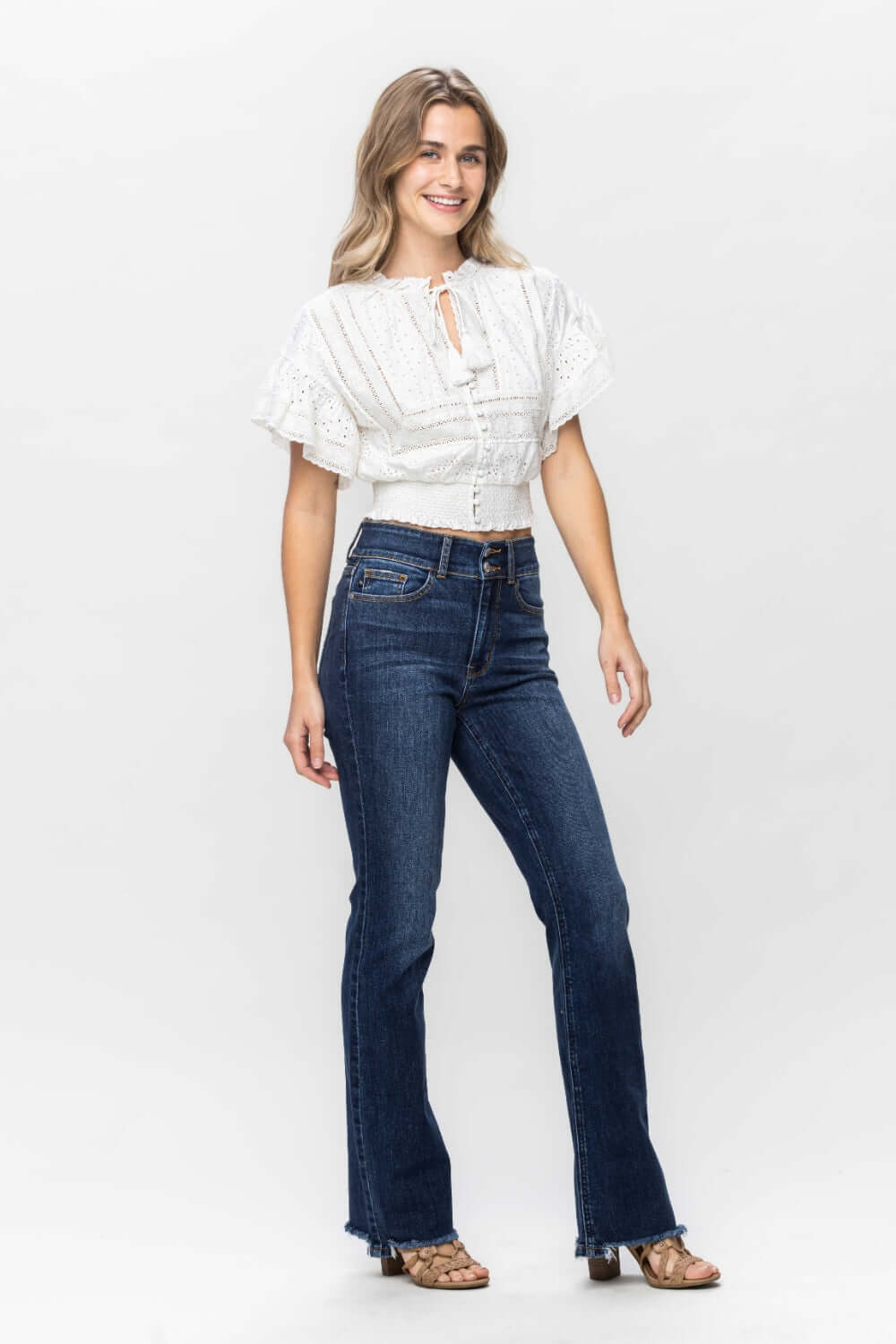 Woman wearing Judy Blue Frayed Hem Bootcut Jeans paired with a white blouse, showcasing trendy and stylish denim fashion.